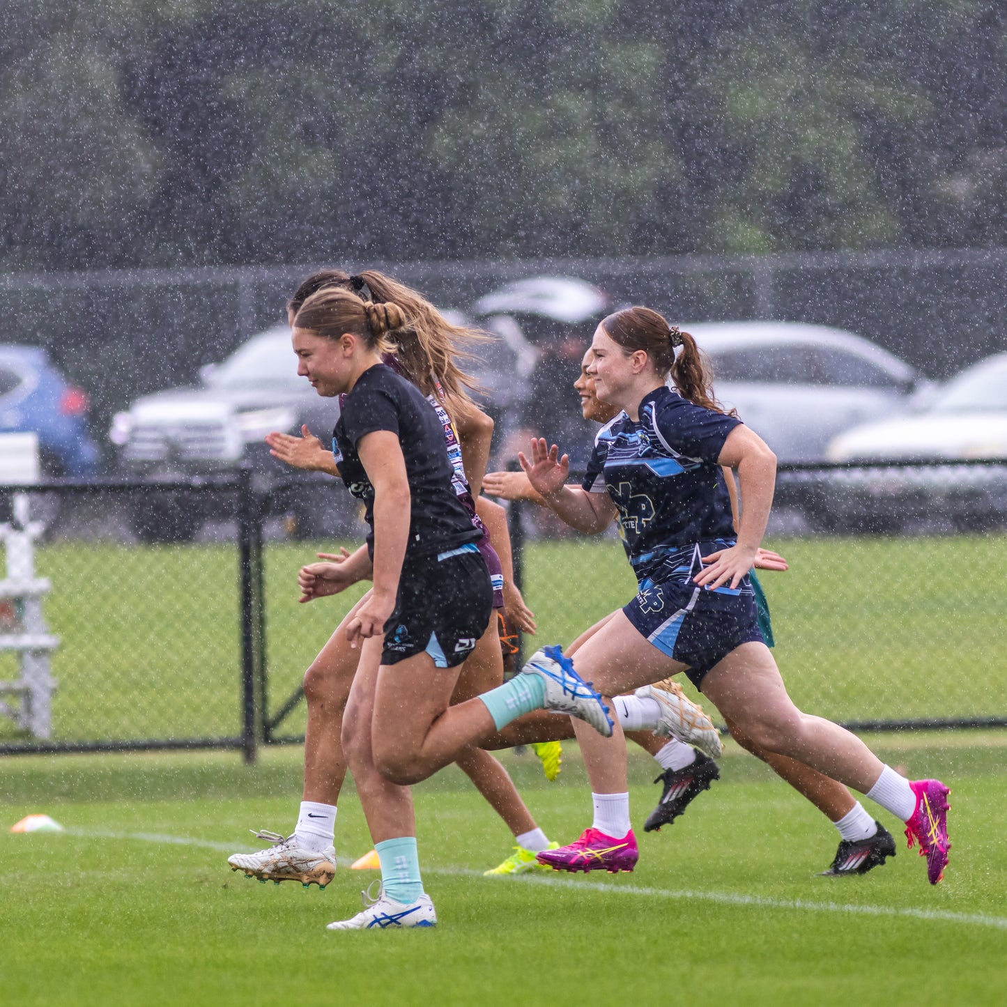 Four young female rugby league players running in the rain
